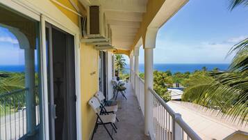 A balcony with a view of the ocean, a seating area with chairs, and a door leading to the interior.