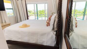 A bedroom with a large bed, a view of greenery through the window, and a wooden headboard.