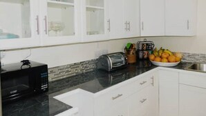 A kitchen with white cabinets, a black microwave, a toaster, and a fruit bowl. - La Kayé Celesté your home away from home!! (Castries)