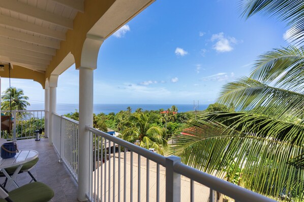 A balcony with a view of the ocean, palm trees, and a clear sky.