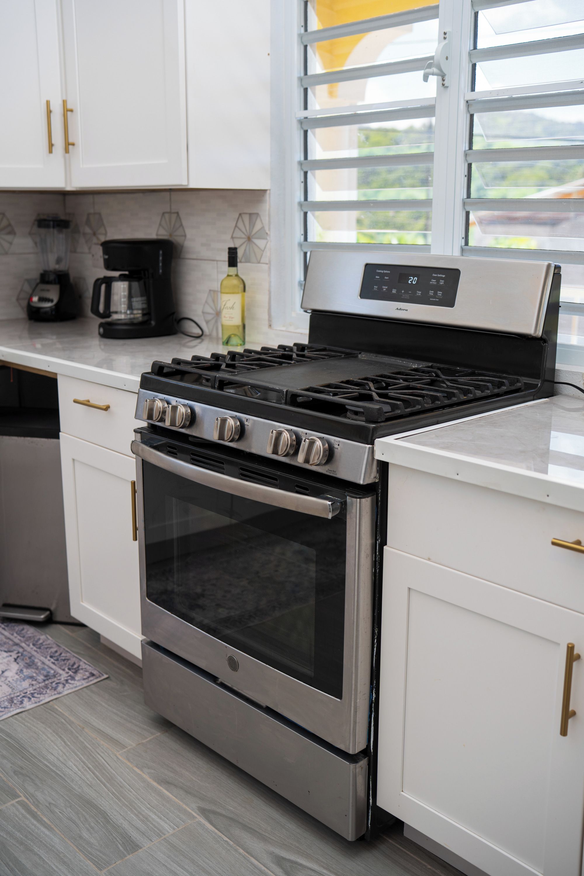 A kitchen with white cabinets, a stainless steel stove, and a window with blinds.