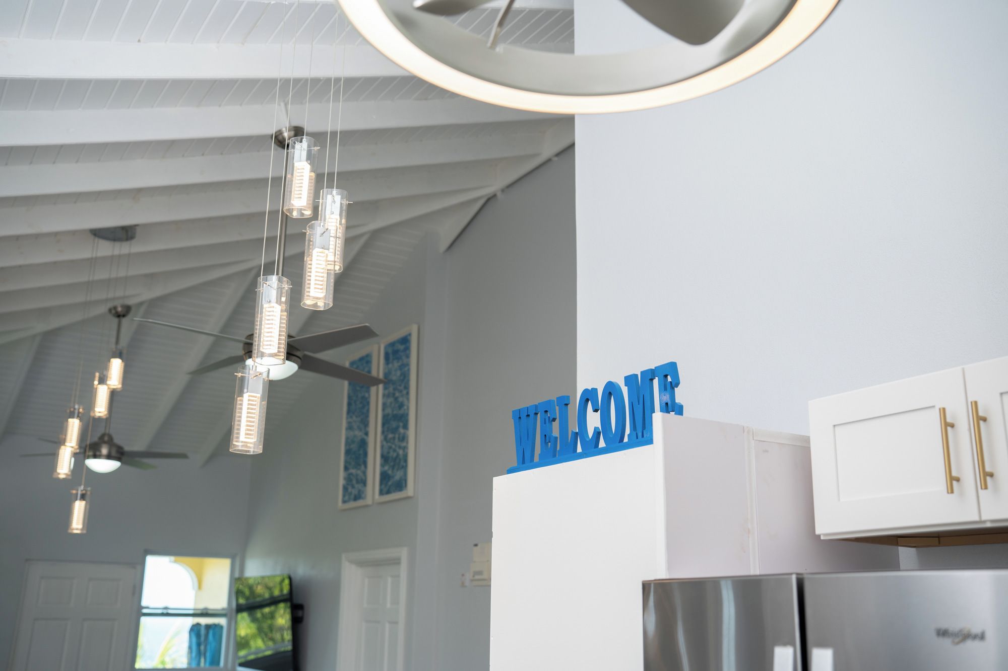A modern kitchen with a 'WELCOME' sign, stainless steel appliances, and pendant lighting.