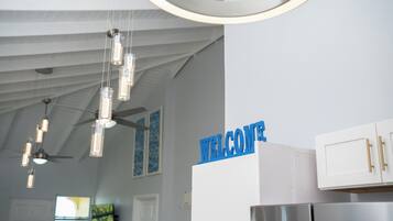 A modern kitchen with a 'WELCOME' sign, stainless steel appliances, and pendant lighting.
