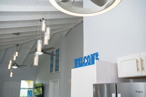 A modern kitchen with a 'WELCOME' sign, stainless steel appliances, and pendant lighting.