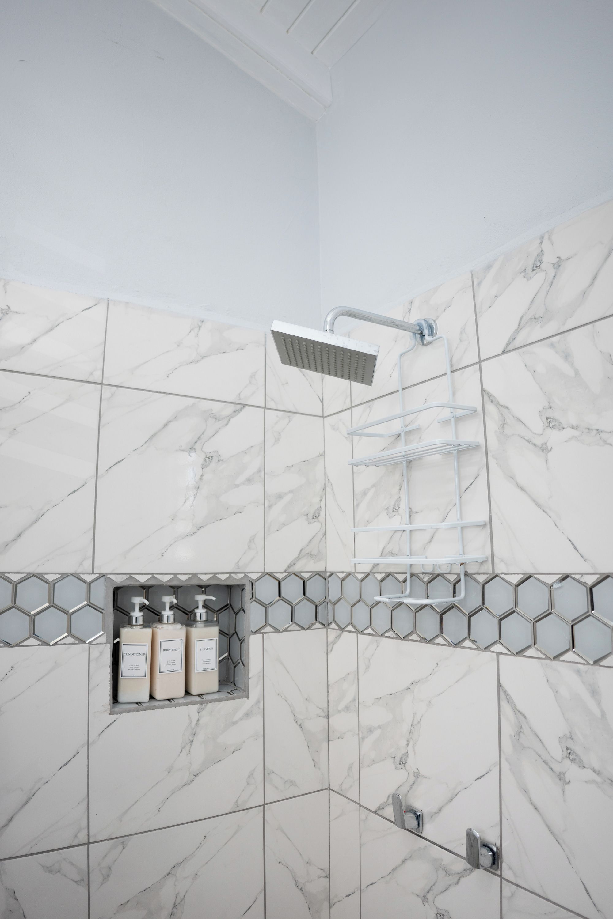 A bathroom with a shower, marble tiles, and a shelf with toiletries.