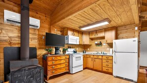 Interior de una cabaña de madera con chimenea, zona de cocina y televisor.