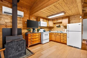 L’intérieur d’un chalet en bois comprend une cheminée, un coin cuisine et un téléviseur.
