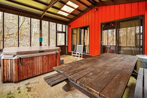 Un espacio al aire libre techado con un jacuzzi, una mesa de madera y sillas.