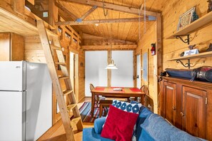 Een houten cabin interieur met een eettafel, een bank, een koelkast en een bel die aan het plafond hangt.