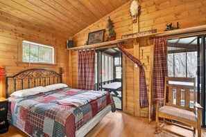 Ein Blockhauskaminareal mit einem Bett, einer hölzernen Bank, einem Tisch und einem Fenster mit Jalousien.