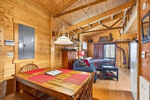 A wooden cabin interior with a dining table, sofa, and a fireplace. - Lazy Lane Cabins - Creekside (Laurelville)