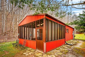 A red wooden cabin with large windows, a stone pathway, and a bench.