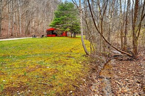 Une zone boisée avec un bâtiment rouge, un champ d’herbe et un ruisseau.