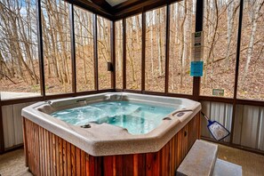 A hot tub in a wooden cabin with a view of a forest.