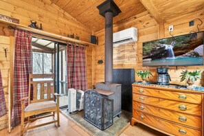 Een blokhutinterieur met een open haard, een televisie, een houten dressoir en een stoel.