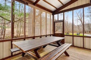 Una mesa de picnic techada con bancos, ventanas amplias y vista a árboles.