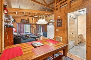 A wooden interior with a dining table, chairs, a sofa, and a kitchen area.