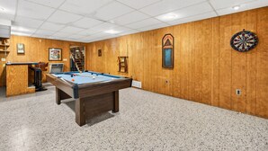 A pool table in a room with wooden walls, a dartboard, and a bar area. - Lazy Lane Cabins - Lane's End (Laurelville)