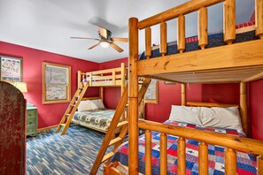 Une chambre avec un lit superposé, une échelle, un ventilateur de plafond et une couvre-lit matelassé.