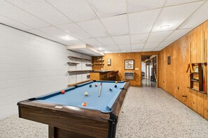 A pool table with balls, a wooden wall, and a hallway leading to another room.