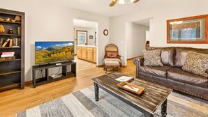 A living room with a television, a brown leather sofa, a wooden coffee table, and a bookshelf. - Lazy Lane Cabins - Lane's End (Laurelville)
