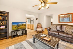 A living room with a television, a brown leather sofa, a wooden coffee table, and a bookshelf. - Lazy Lane Cabins - Lane's End (Laurelville)