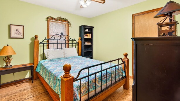 A bedroom with a bed, a ceiling fan, a nightstand, a lamp, a bookshelf, and a mirror. - Lazy Lane Cabins - Lane's End (Laurelville)