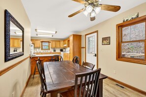 A kitchen with wooden cabinets, a dining table with chairs, a ceiling fan, and a window with a view. - Lazy Lane Cabins - Lane's End (Laurelville)