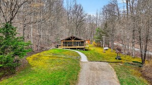 A lodge with a deck, surrounded by trees, and a gravel path leading to it. - Lazy Lane Cabins - Lane's End (Laurelville)