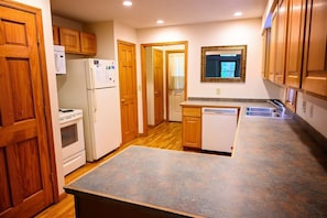 A kitchen with wooden cabinets, a refrigerator, an oven, a dishwasher, and a countertop. - Lazy Lane Cabins - Tree-Top Chalet (Logan)