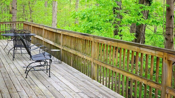 Une terrasse en bois, agrémentée de chaises et de tables en métal, entourée d’une rambarde en bois, et offrant une vue sur une forêt.