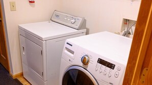 Une buanderie équipée de deux machines à laver, d’un extincteur et d’une étagère contenant des produits de nettoyage.