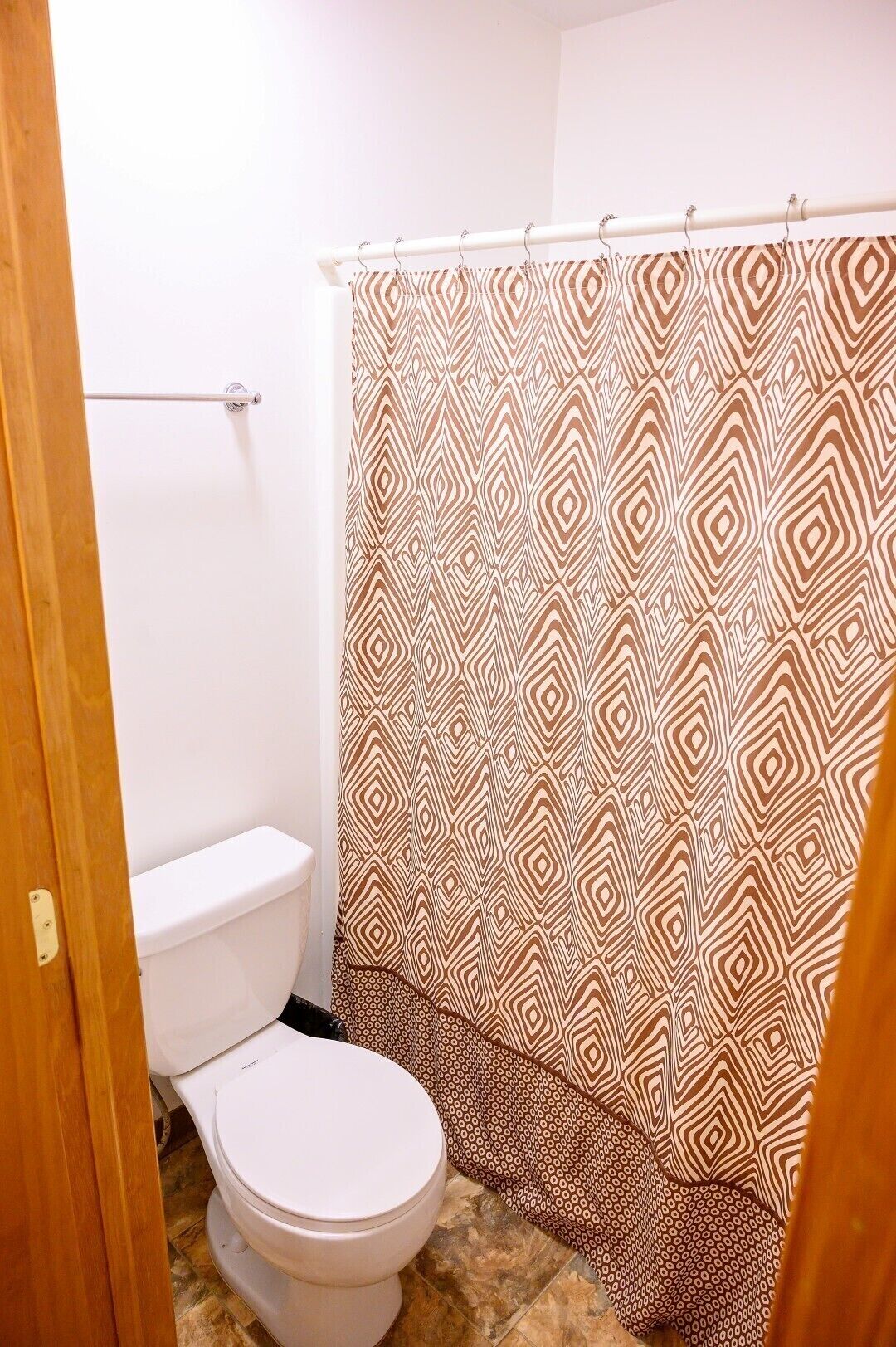 Une salle de bain avec un rideau de douche à motifs, des toilettes blanches et une porte en bois.