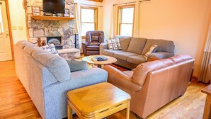 Ein gemütliches Wohnzimmer mit Kamin aus Stein, Ledersofas und einem Fernseher.