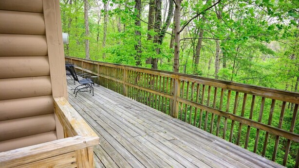 Eine Holzterrasse mit Geländer, einer Bank und einem Tisch, umgeben von einem Wald.