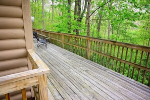 Une terrasse en bois, dotée d’une rambarde, d’un banc et d’une table, entourée d’une forêt.
