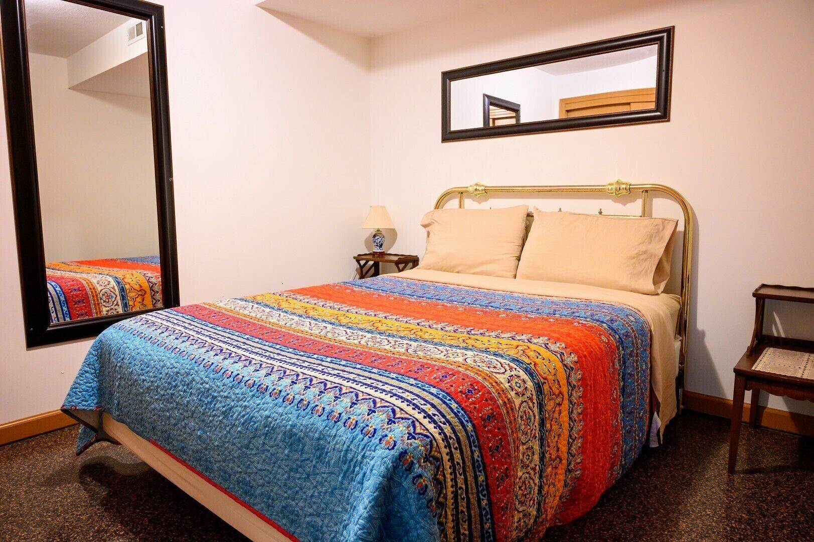 A bed with a colorful quilt, a bedside lamp, and a mirror on the wall.