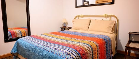 A bed with a colorful quilt, a bedside lamp, and a mirror on the wall.