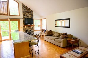 A spacious living area with a stone fireplace, a large window, and a kitchen with a granite countertop.