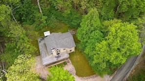 An aerial view of a house surrounded by dense green forest, with a visible deck and a satellite dish.