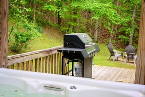 Un jacuzzi en una terraza de madera con una parrilla y asientos exteriores.