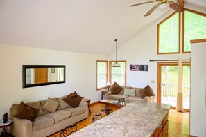 A spacious living area with a large sofa, a dining table, and a ceiling fan.