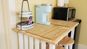 Una encimera de cocina con cafetera, microondas y una bandeja con crema para café.