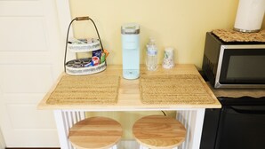 Una cocina con microondas, hervidor de agua, botella de agua y un estante con aperitivos.