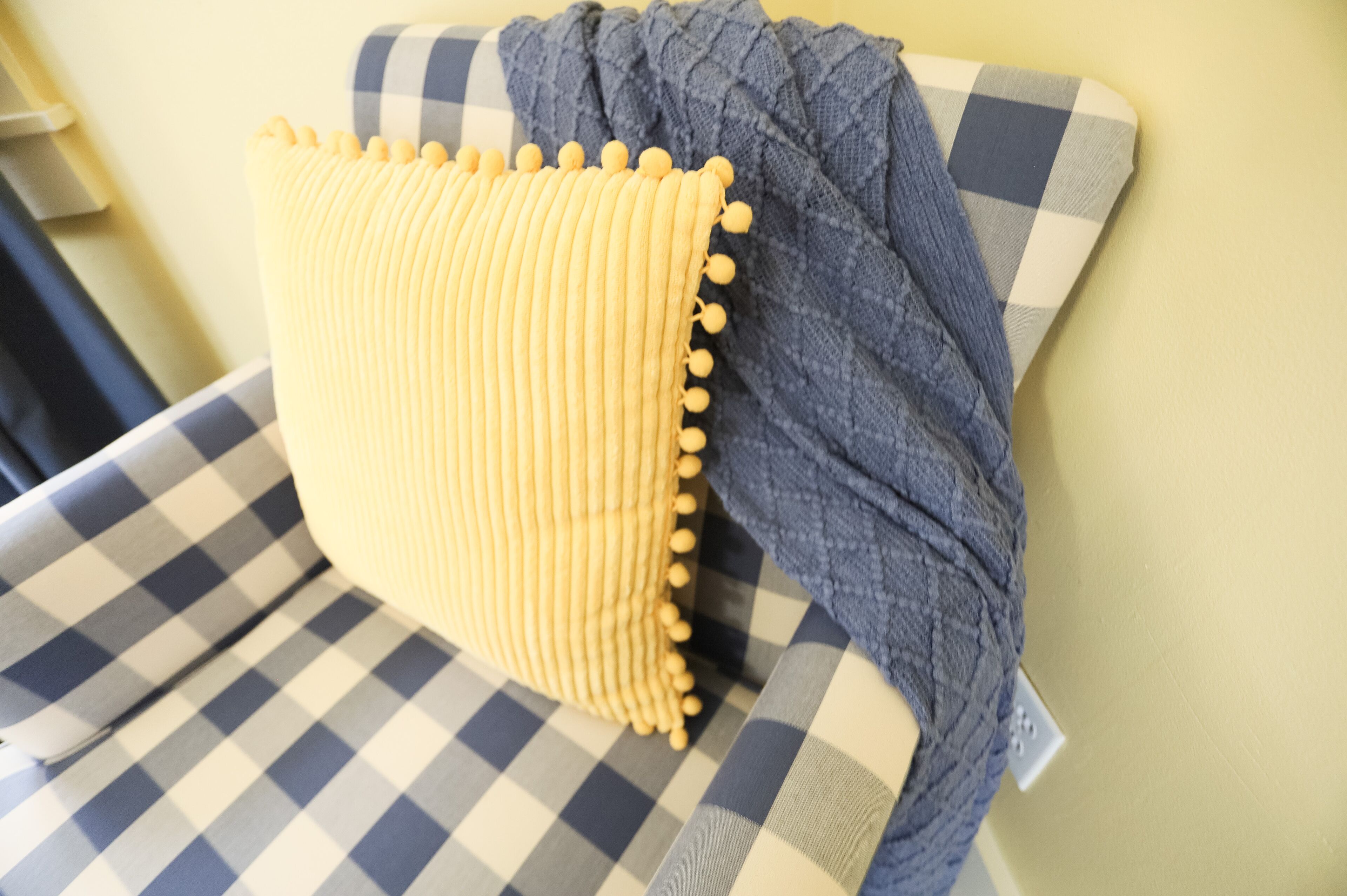 Un sofá a cuadros con un cojín amarillo y una manta de punto azul.