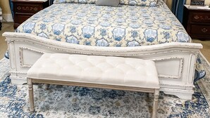 Un dormitorio con cama, mesita de noche, lámpara, un arreglo en la pared y una ventana con cortinas.