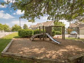 A playground with a slide and climbing structure surrounded by a wooden border and mulch, set in a residential area with houses in the background. - Peak Hangout * Studio Loft for 4 * Deck Wifi Pool (Gatlinburg)