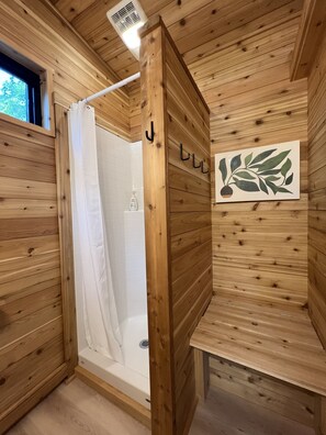 A wooden cabin bathroom with a shower, a white bathtub, and a wooden shelf with a leaf decoration.