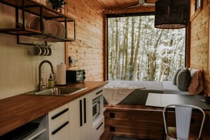 Cocina compacta con armarios de madera, un lavamanos y una ventana con vista a un bosque.