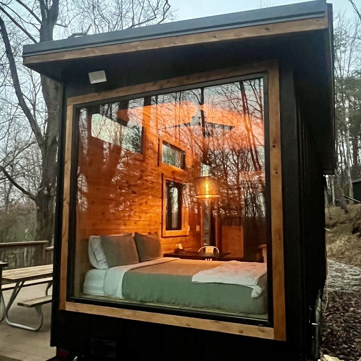 Una piccola cabina chiusa con un letto, un tavolo e una lampada a sospensione.
